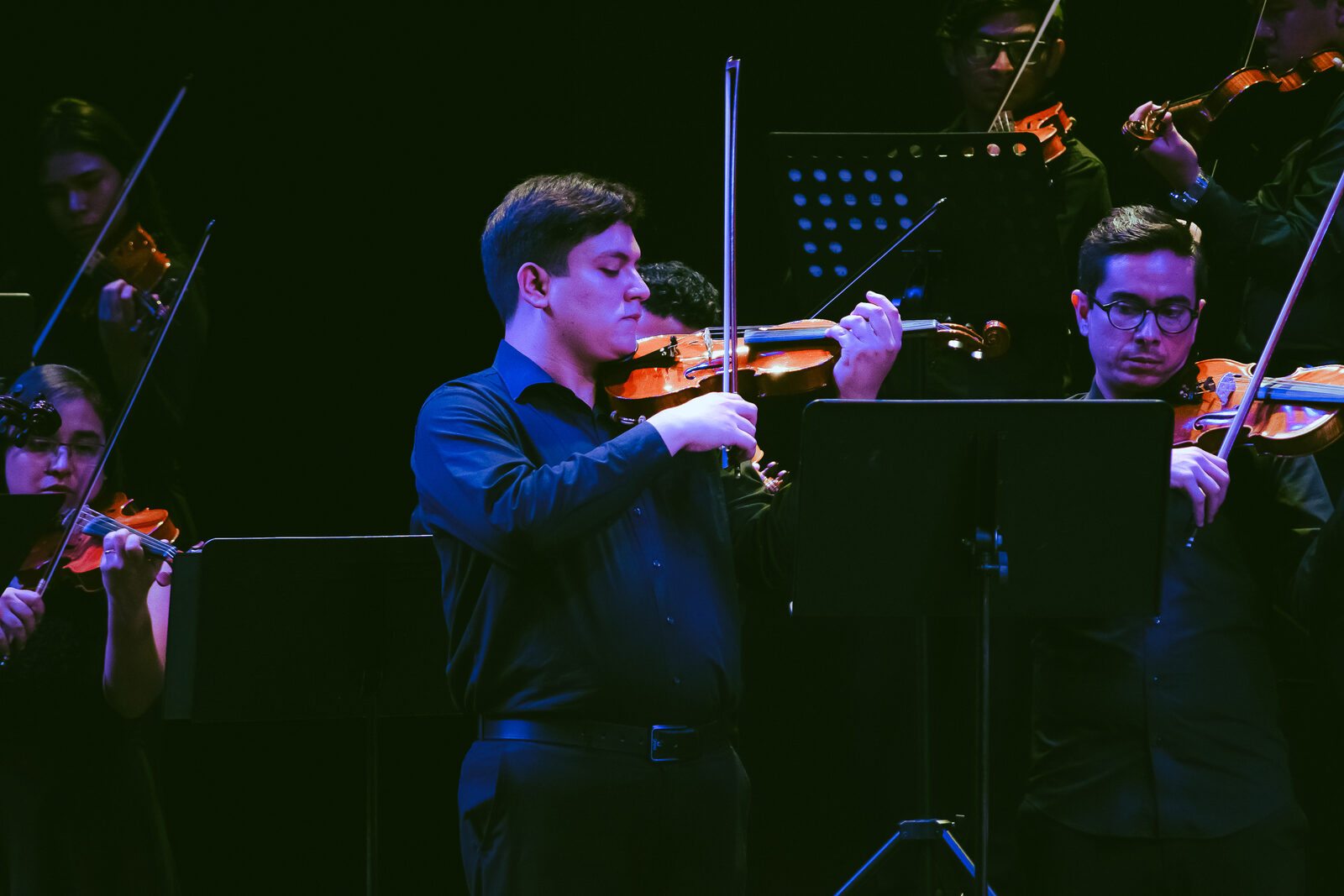 Violinista de la Sociedad tocando de pie frente a la orquesta de cámara, con vestuario formal negro